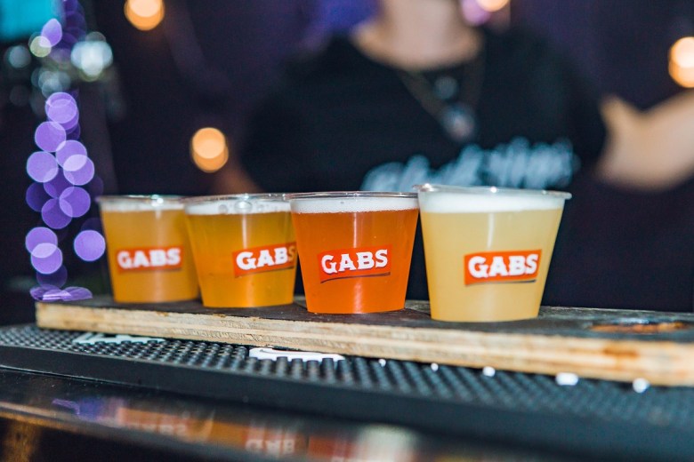 Four colorful craft beers served in plastic cups on a wooden board